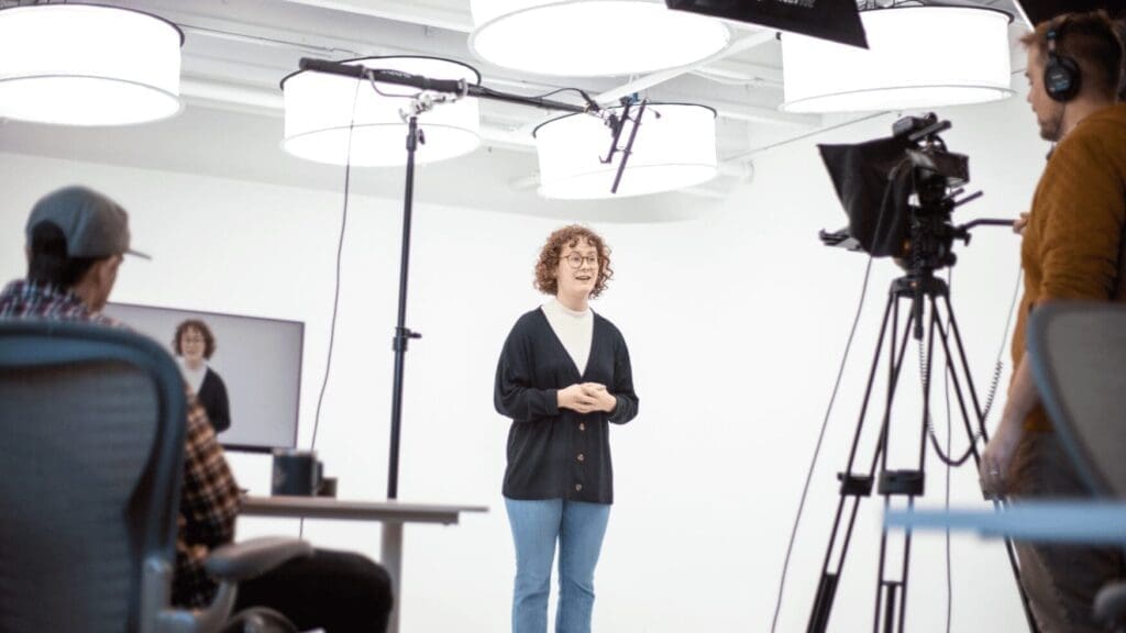 A woman stands in front of a camera with two men seated in front of her at Tellwell Studio in Fargo.