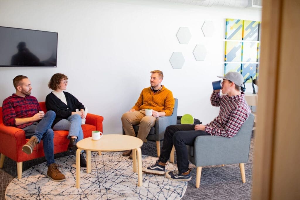 Tellwell Studio stock photo showing the team sitting in a circle with a desk in between.