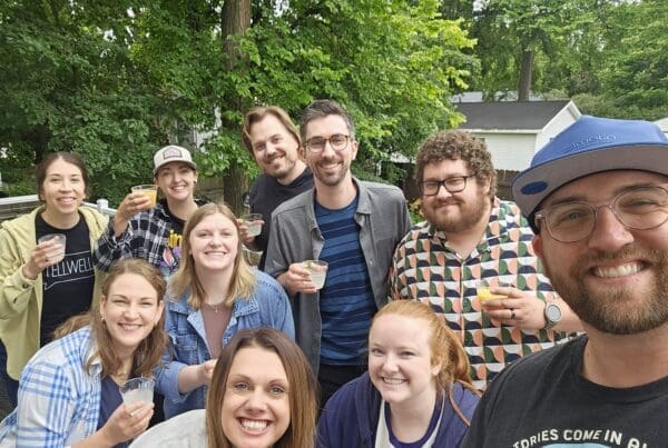 A group poses for a photo, each holding a glass filled with juice. They are outdoors.