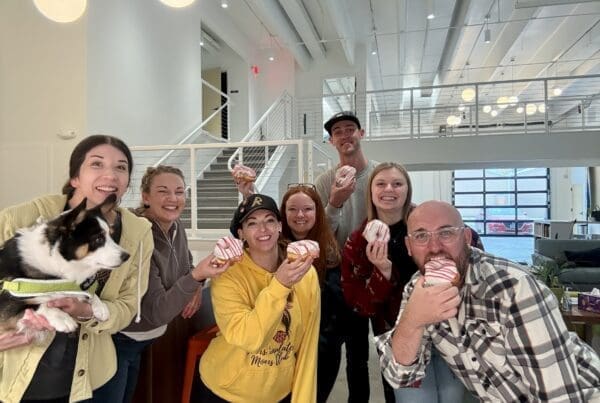 A group of seven people smile for a photo while each holding a donut.
