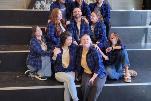 A candid shot of the same ten-person team in blue flannels sitting on black stairs. They are laughing and looking at one another in a relaxed, informal pose.