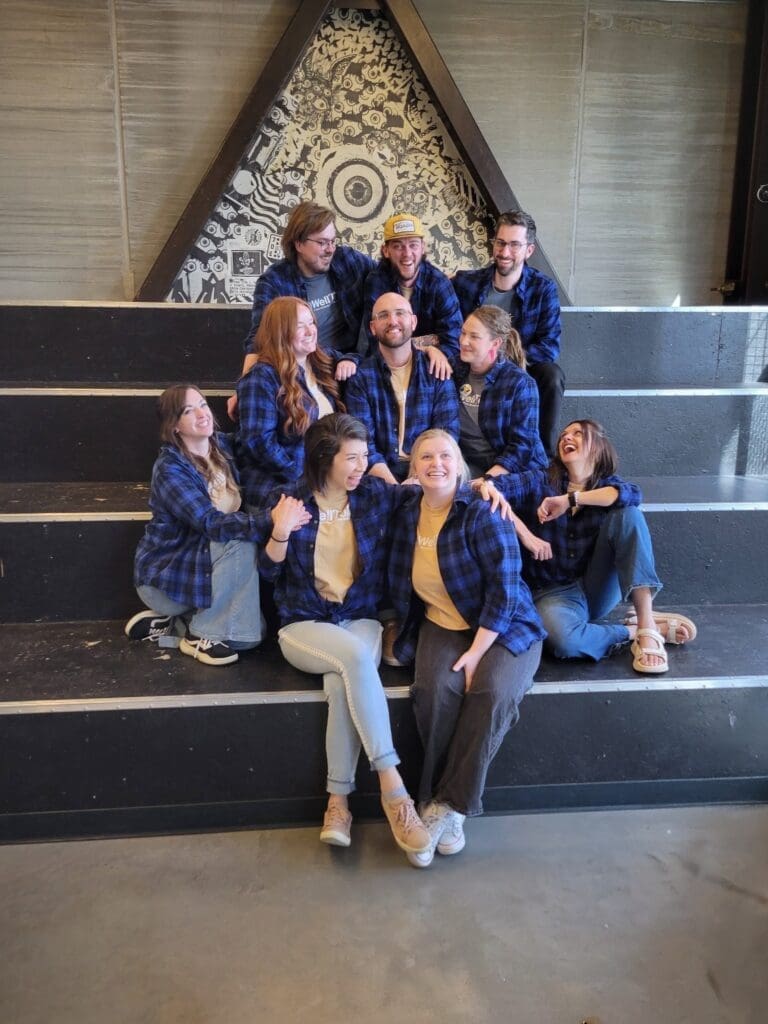 A candid shot of the same ten-person team in blue flannels sitting on black stairs. They are laughing and looking at one another in a relaxed, informal pose.